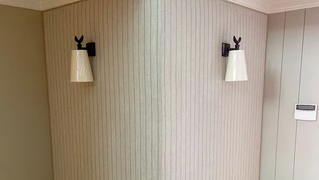 Innebygd hjørnebenk med tapet på veggene og vegglamper montert over sitteplassen.