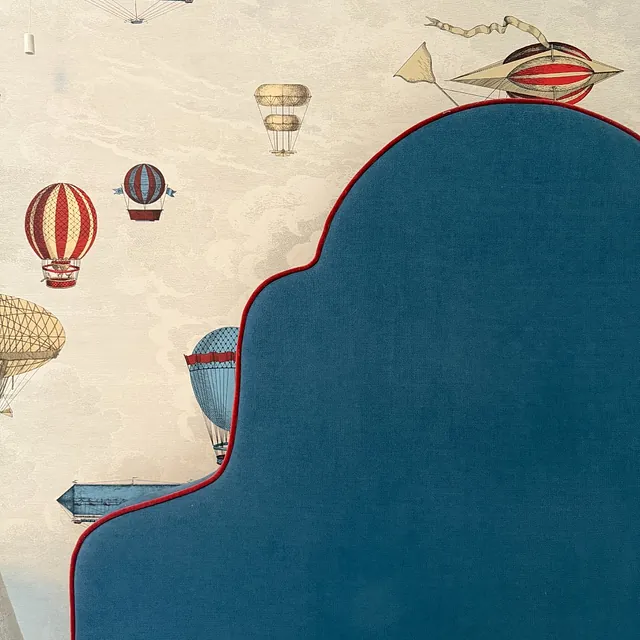 Blå polstret sengegavl med bølgende toppkant mot tapet med dekorativt motiv.