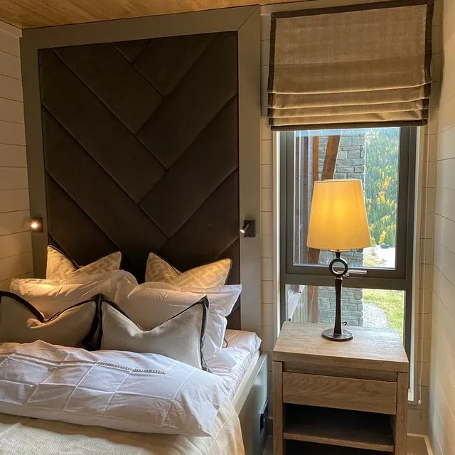 Seng med mørk polstret sengegavl i fiskebeinsmønster og dekorative puter.